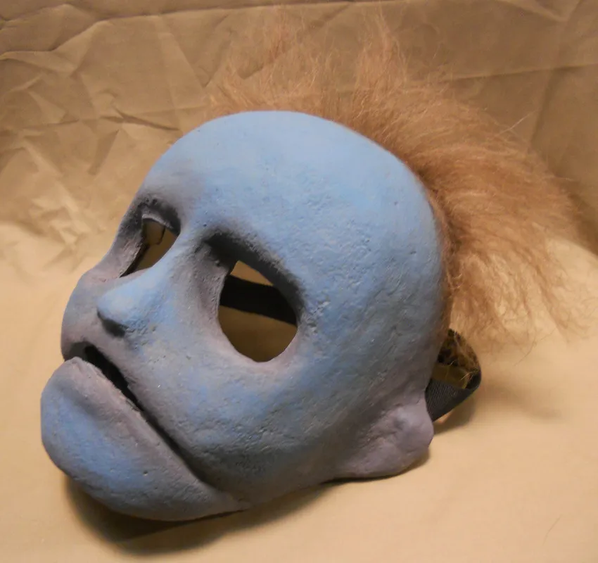 The limited-edition mask reproduction with attached hair and head strap, resting on tan fabric